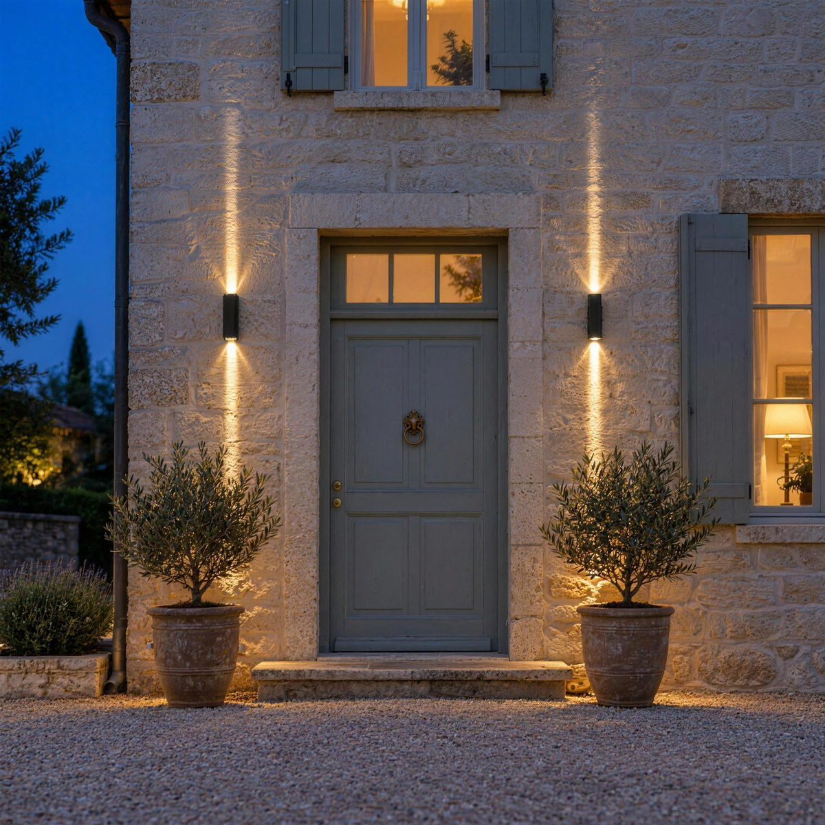 Deux appliques murales extérieures LED noires allumées de part et d'autre d'une porte d'entrée, faisceaux vers le haut et vers le bas, à la tombée de la nuit