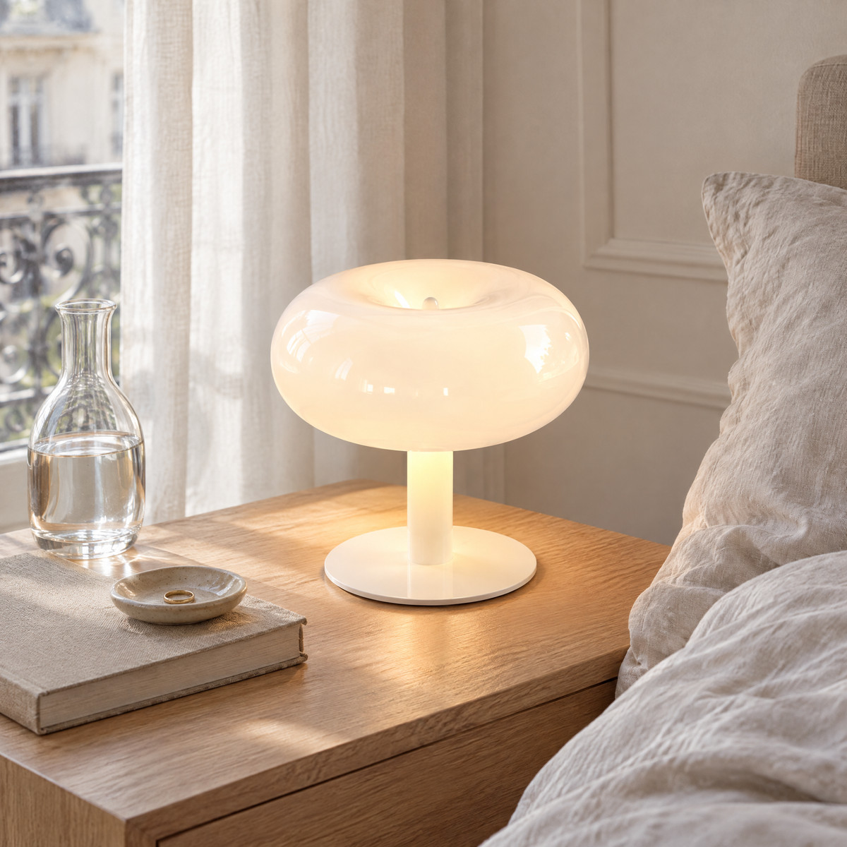 Lampe champignon blanche allumée sur une table de chevet en chêne