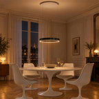 Suspension anneau LED noire allumée au-dessus d'une table ronde blanche, salle à manger le soir
