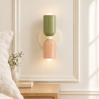 Applique murale macaron vert sauge et rose allumée au-dessus d'une table de chevet