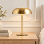 Lampe de chevet champignon en métal doré allumée sur une table de chevet en chêne