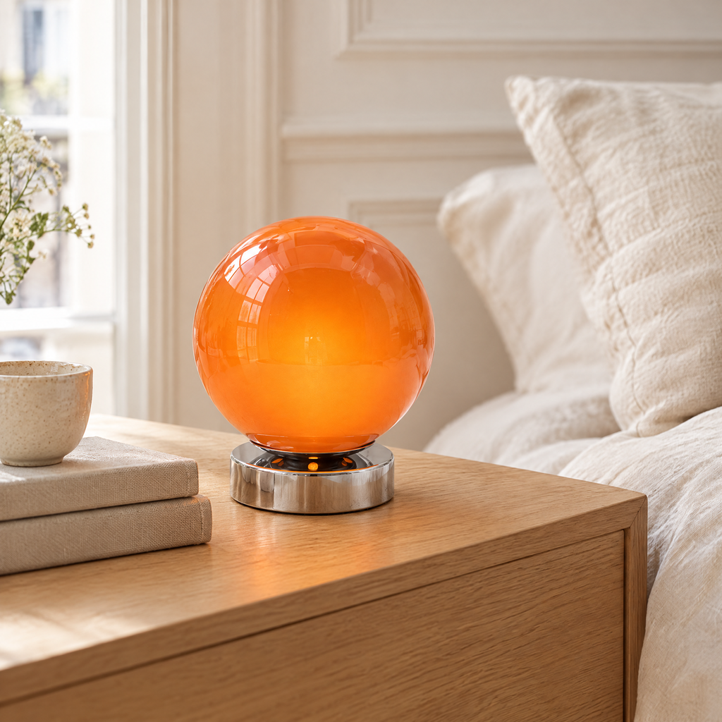 Lampe de chevet boule en verre orange allumée sur une table de chevet en chêne